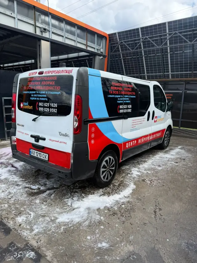 Біло-червоний мікроавтобус Renault Trafic з написами «Транспортування лежачих хворих та осіб з інвалідністю» і «Центр нейрореабілітації», сфотографований ззаду на майданчику.