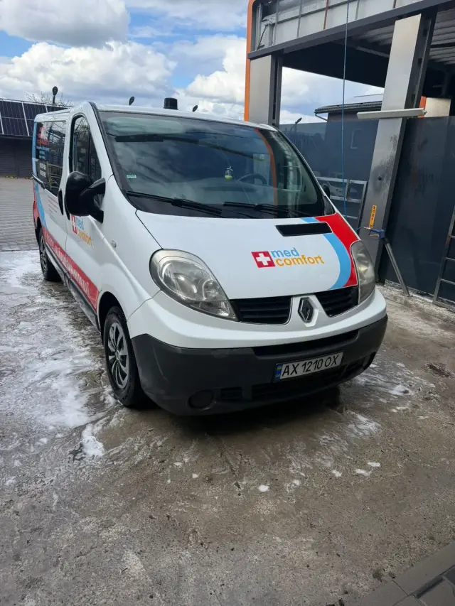 Мікроавтобус Renault з логотипом med comfort на капоті, сфотографований спереду на автомийці; на асфальті довкола видно мильну піну.