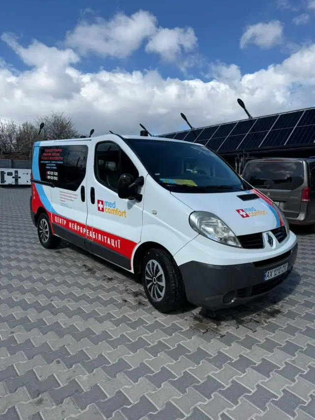 Білий санітарний мікроавтобус із логотипом med comfort та червоною смугою «Центр нейрореабілітації» стоїть на брукованому майданчику під блакитним небом із хмарами.